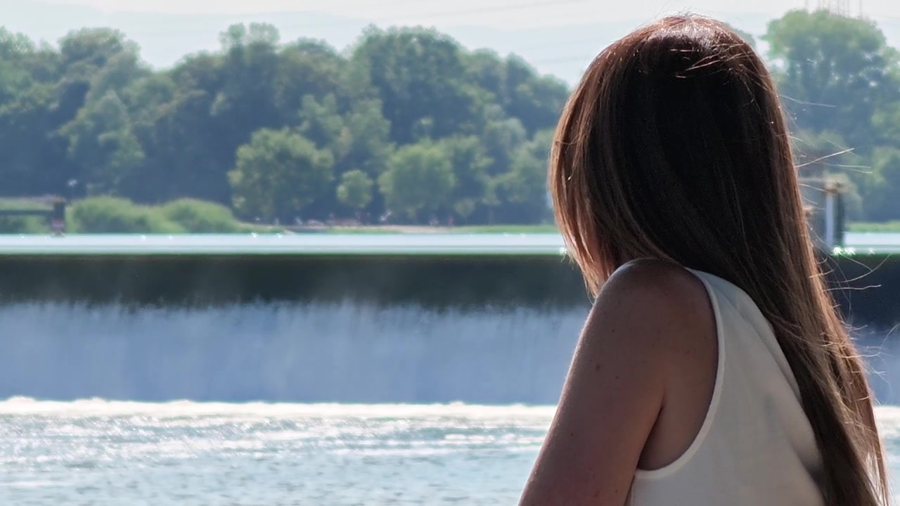 Woman with long hair contemplating the Breisach agricultural dam on the Rhine River on a sunny day