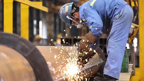 steelworker polishing weld spots on a steel column using a grinder