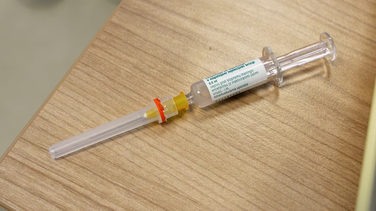 Vaccine vial and syringe on doctor’s desk, tick-borne encephalitis (TBE) vaccine used for intramuscular injection, medium shot