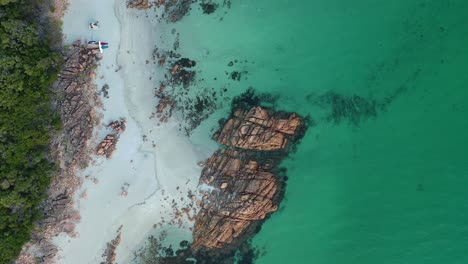 Aerial-view-of-hidden-seciuded-white-sand-Castle-Rock-beach-and-rock-formations-by-tropical-rainforest,-birdseye-top-down-rising-drone-shot