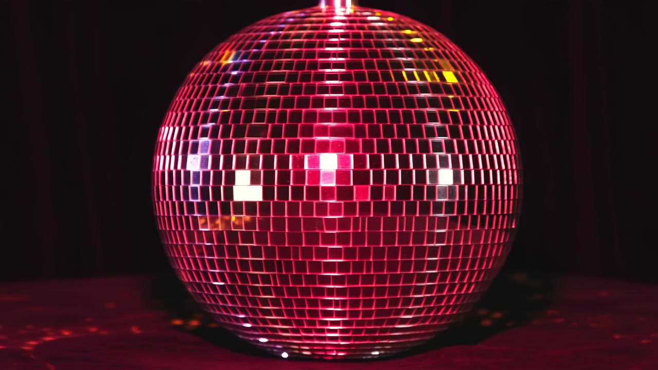 Primo piano di una palla da discoteca a specchi con piccole tessere quadrate che riflettono luci rosa e magenta saturi su un palco scuro, con riflessi luminosi, contrasto profondo, bagliore rosso sul pavimento e un'atmosfera retrò vivace.
