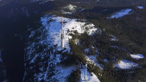 aerial tracking shot of a wind turbine and a broadcast tower on a snow covered plateau