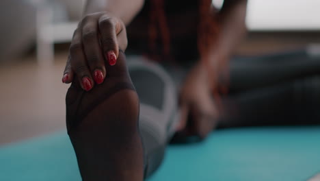 Close-up-of-black-athlete-sitting-on-floor-on-mat-with-leg-spread