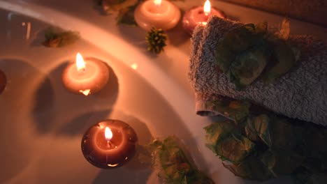 relaxing spa background with candles floating in the bath water, some green petals and a towel near the water surface