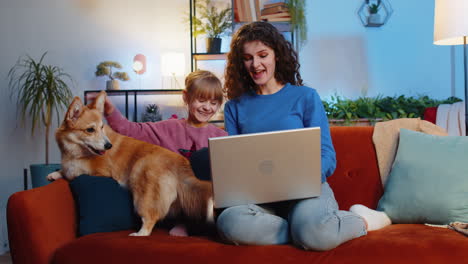 madre y hija niña usando portátil al lado de un lindo perro corgi en el sofá viendo una película