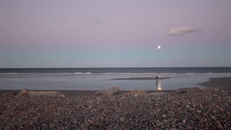 moonrise over a beach on the atlantic while a couple walks across the sand