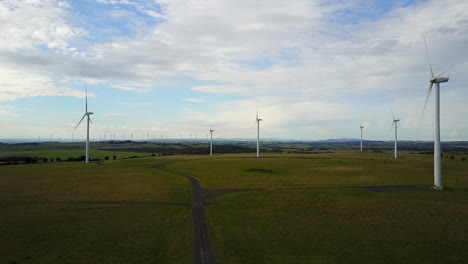 AERIAL---Drone-footage-of-windfarm-moving-slowly-towards-turbines-with-blue-sky-and-clouds-over-farmland