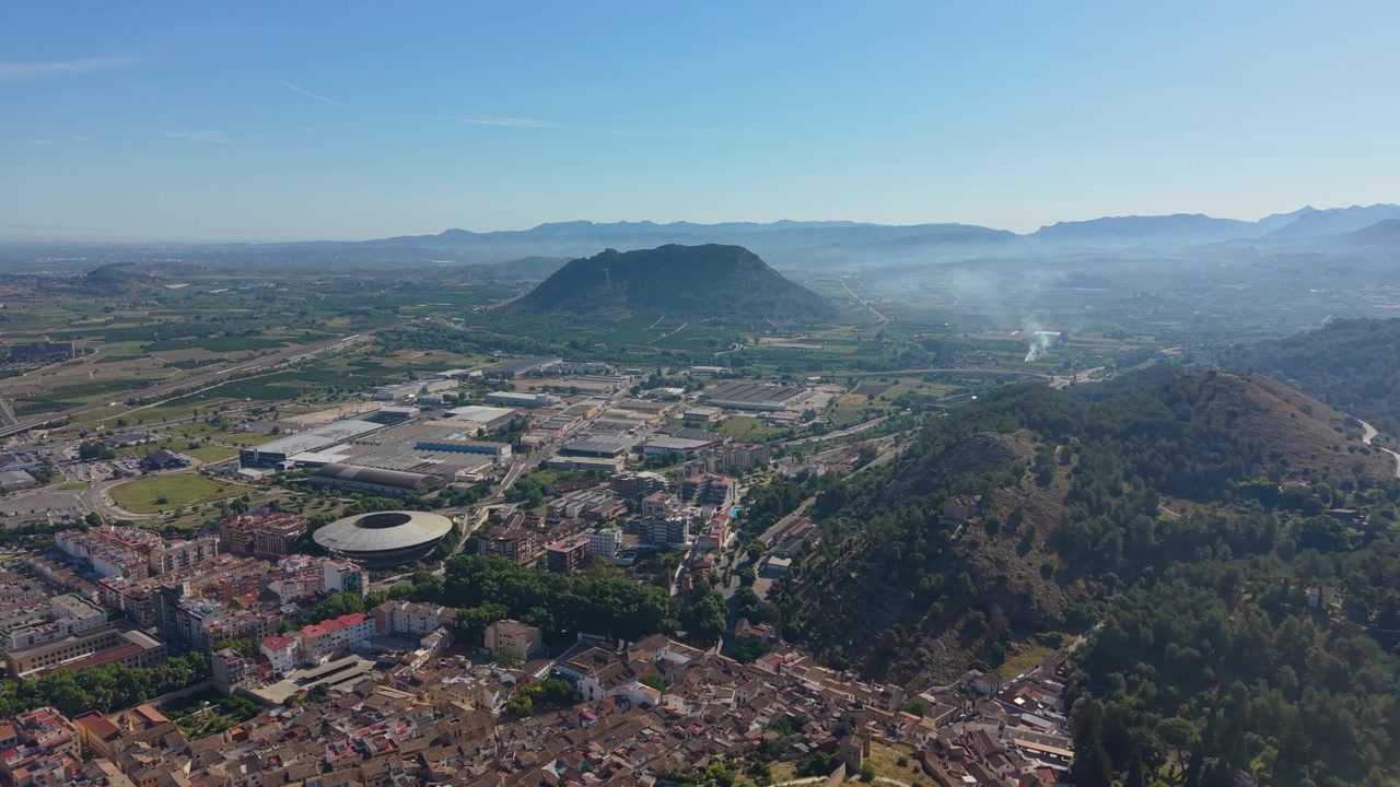 Panorama aereo con drone su Xàtiva, Spagna, che mostra la città storica, le valli circostanti, il paesaggio agricolo e le catene montuose distanti.