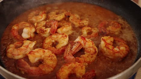 delicious peeled shrimps simmering and boiling on hot pan, reducing and absorbing juicy flavours of red paprika spice with aromatic smokes flowing in the atmosphere, cooking seafood cuisine