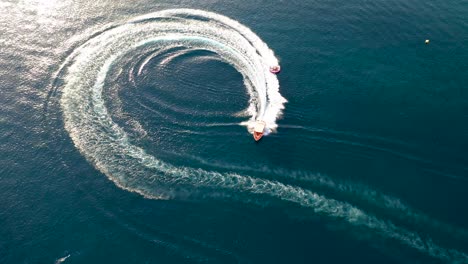 top down view of speed boat towing a big ski or wakeboard turning in a circle against a deep blue water background