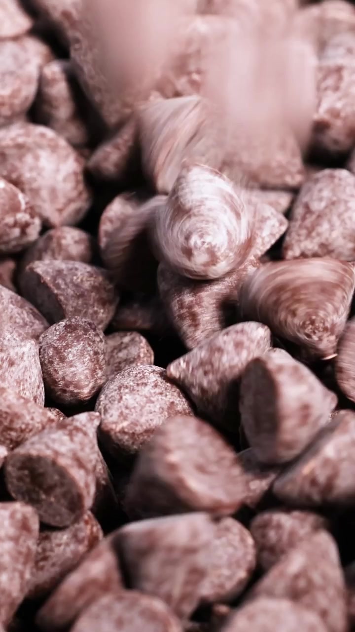 A vertical macro shot of brown chocolate morsels cascading into a growing pile of sweets.