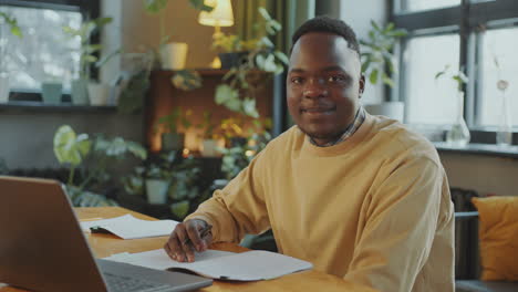 portrait of young black student at desk with laptop and copybooks