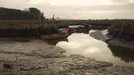 4K-old-wood-fishing-boat-stranged-on-the-muddy-banks-of-a-low-tide-river-with-some-water-flowing-down