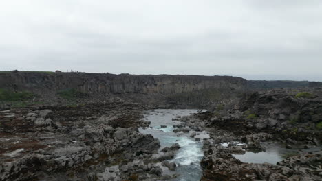 Drone-view-flying-through-water-flowing-on-river-of-Skjálfandafljót-with-rock-and-basalt-formations.-Aerial-view-of-Aldeyjarfoss-waterfall-situated-in-the-northern-part-of-icelandic-highlands