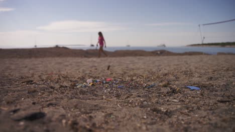 microplástico en la playa, una mujer y un perro pasando al fondo