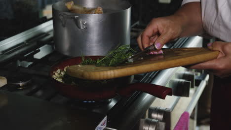 pushing chopped herbs from chopping board into pan on kitchen cooker