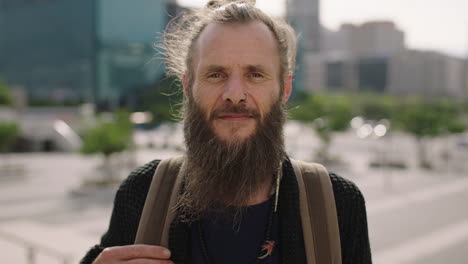 close up portrait of mature hippie man with beard looking at camera confident pensive in sunny urban city background