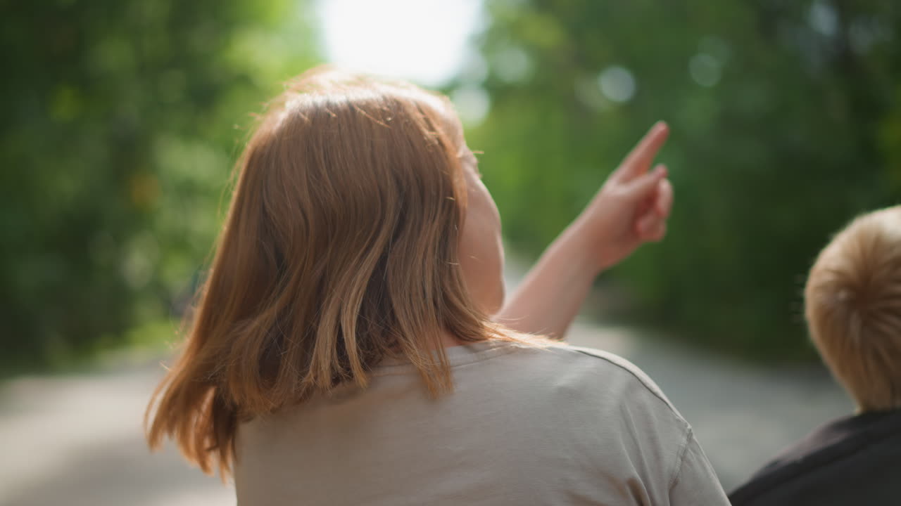 Young Siblings Explore Peaceful Summer Day, Brothers And Sisters Observing Leafy Pathway Under Warm Sunlight, Two Children Look Down Verdant Road While Enjoying Tranquil Summer Walk Together