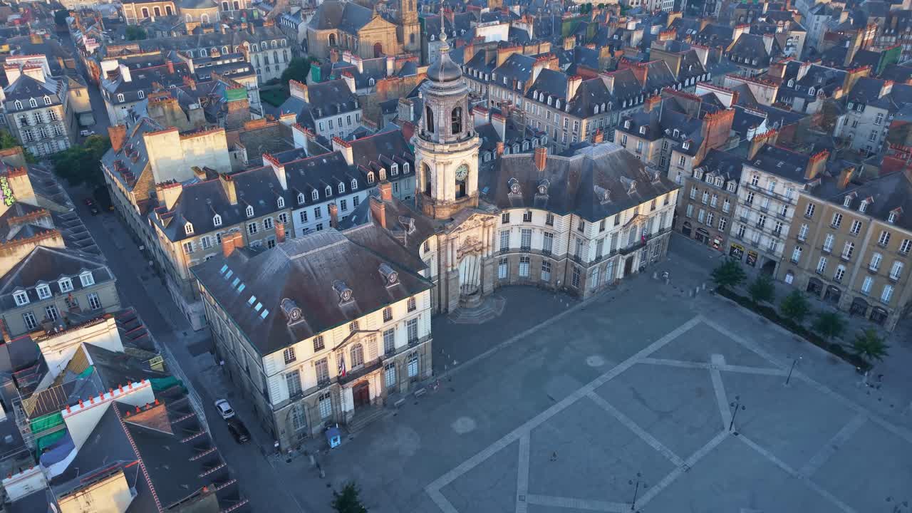 Ripresa aerea in avanti con drone su Piazza del Municipio di Rennes all'alba, che mostra lo storico municipio, la piazza vuota e i tetti circostanti nella luce del primo mattino