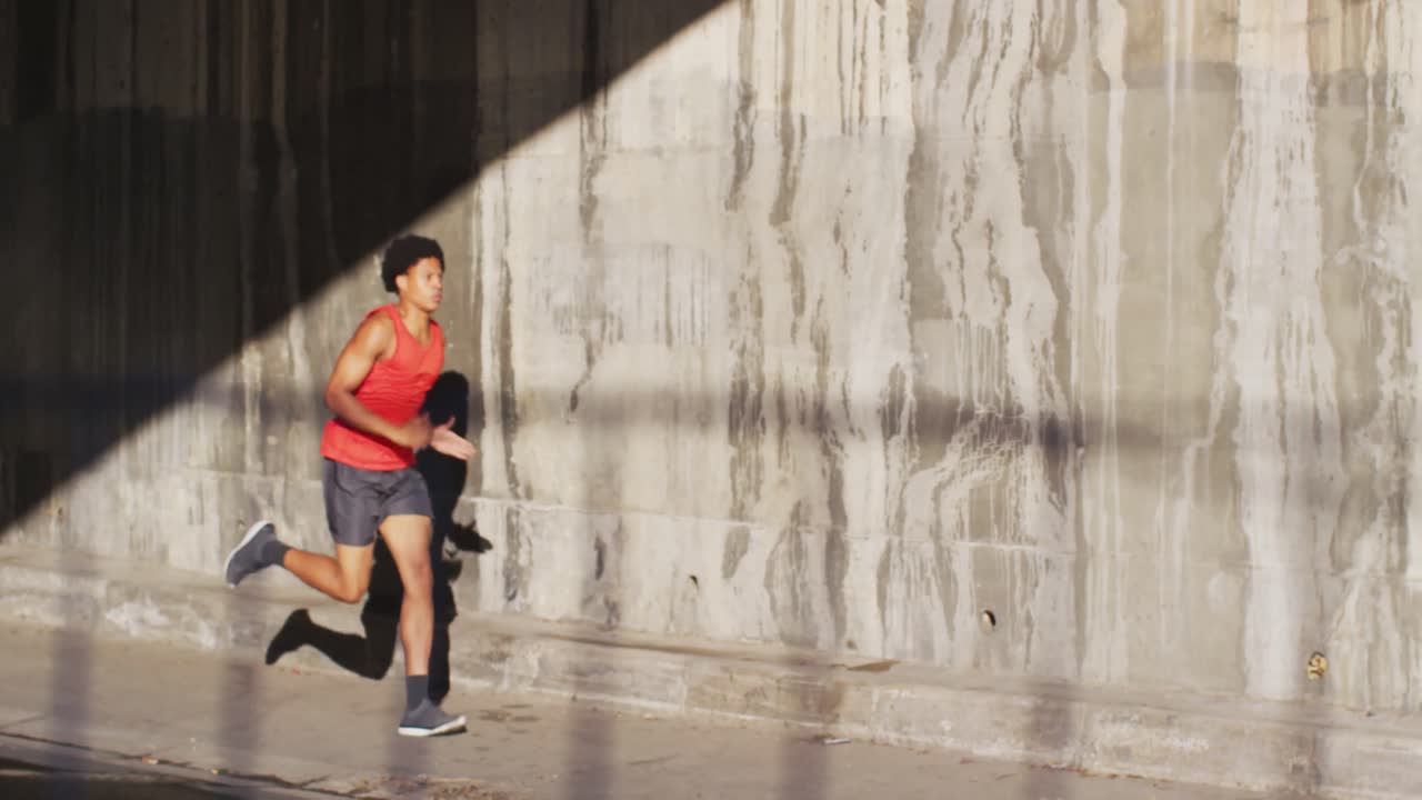 Fit african american man exercising in city, running under bridge