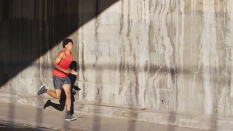 fit african american man exercising in city, running under bridge