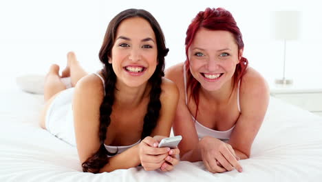 cheerful laughing women holding a smartphone lying on bed