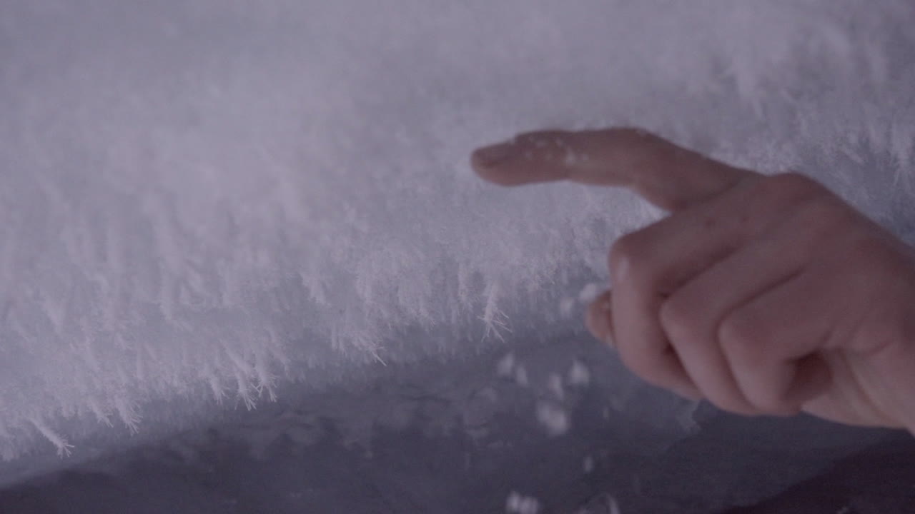 사람이 얼음 결정을 긁어 손가락으로 벗겨내고, 스위스 알프스의 동굴