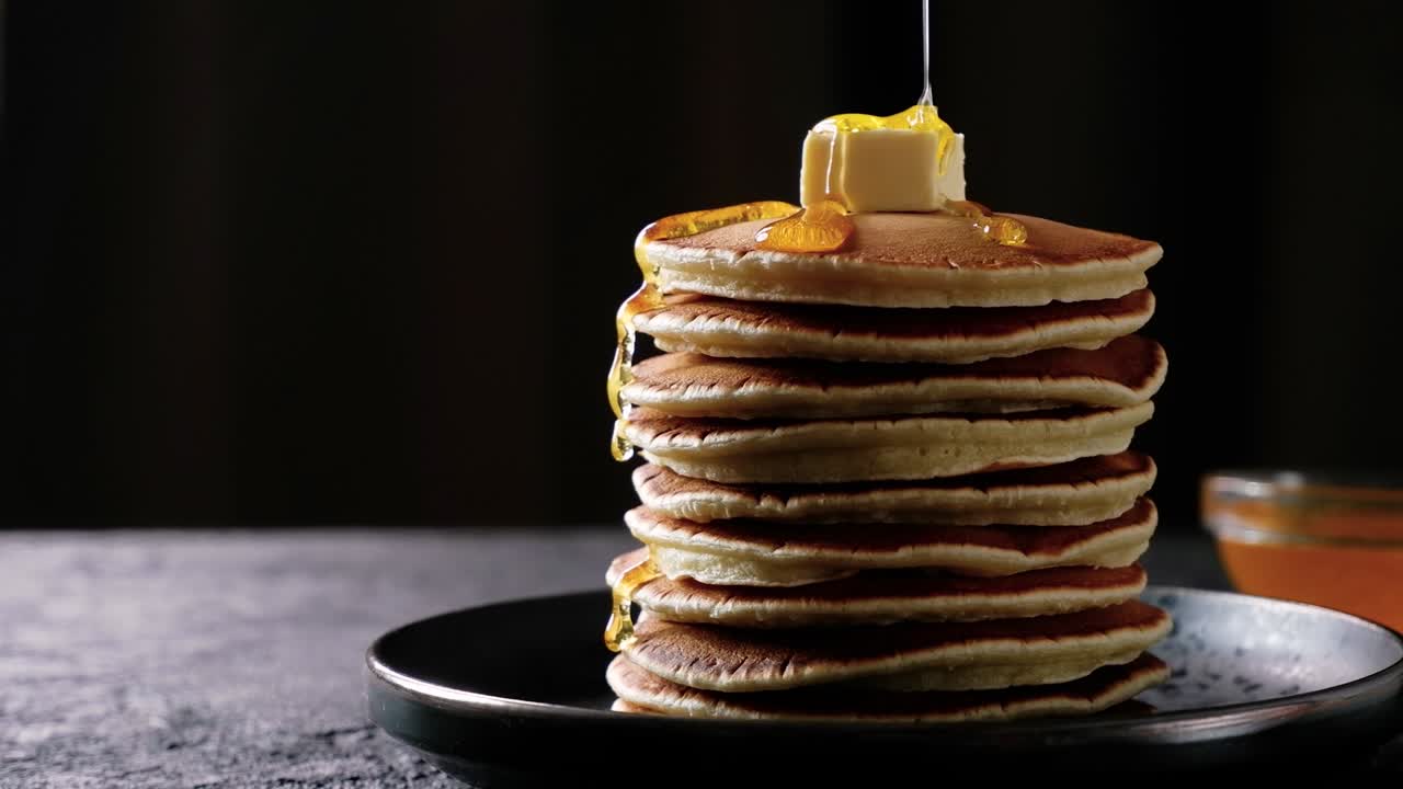 또는 메이플 시럽은 어두운 배경에 버터와 함께 팬케이크의 더미에 부어집니다.