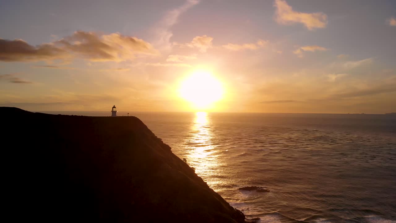 faro de cape reinga con puesta de sol dorada reflejada en el océano en la isla norte, nueva zelanda