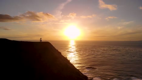 Leuchtturm-Von-Cape-Reinga-Mit-Goldenem-Sonnenuntergang,-Der-Sich-Im-Meer-Auf-Der-Nordinsel,-Neuseeland,-Spiegelt