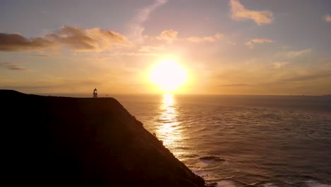 Faro-De-Cabo-Reinga-Con-Puesta-De-Sol-Dorada-Reflejada-En-El-Océano-En-La-Isla-Norte,-Nueva-Zelanda