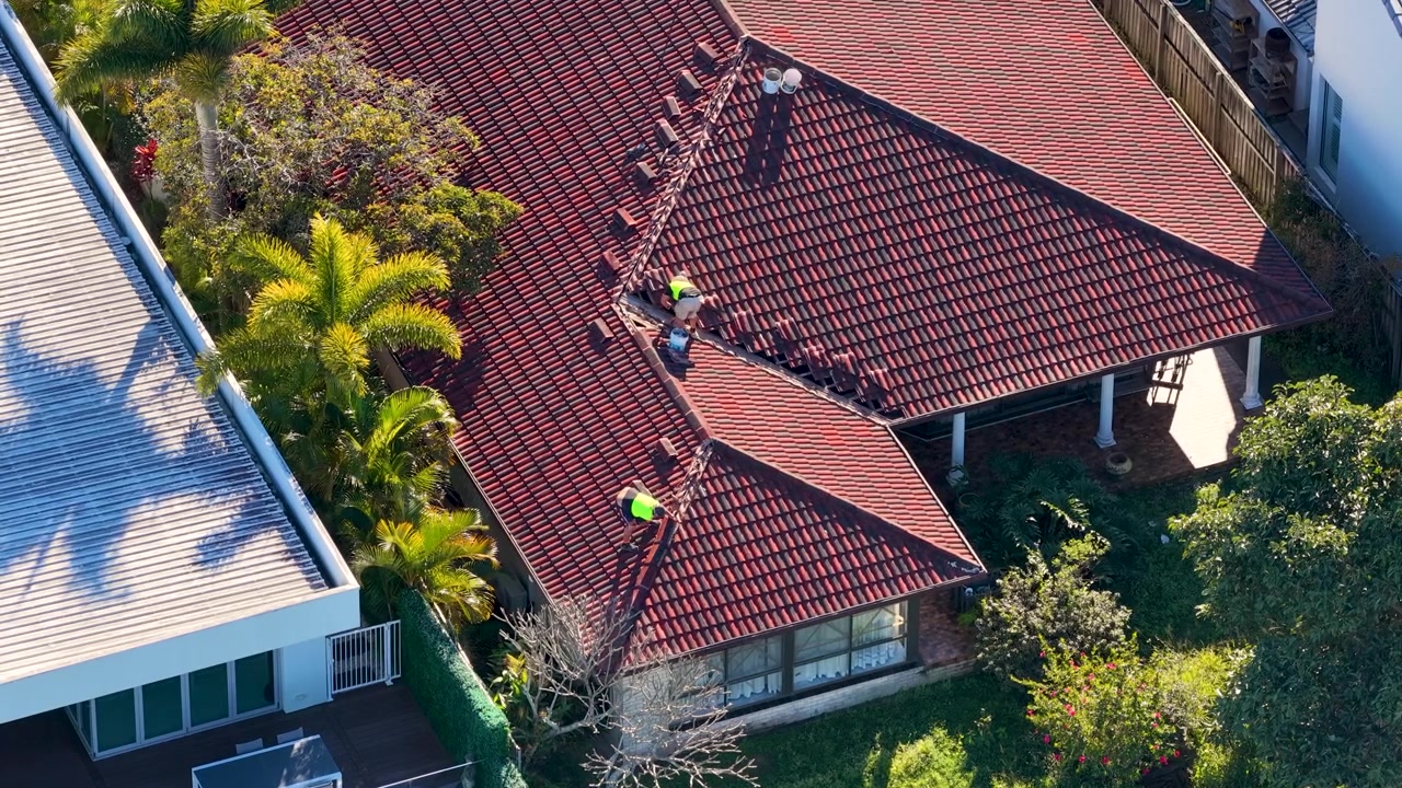Aerial shot of contractors in high-visibility vests performing maintenance on a residential tile roof.