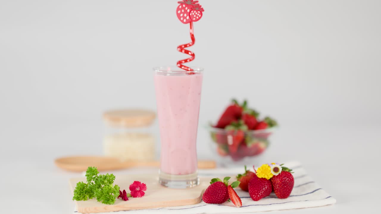 Hand inserts red spiral straw into creamy strawberry milkshake, bright studio lighting, fresh strawberries nearby