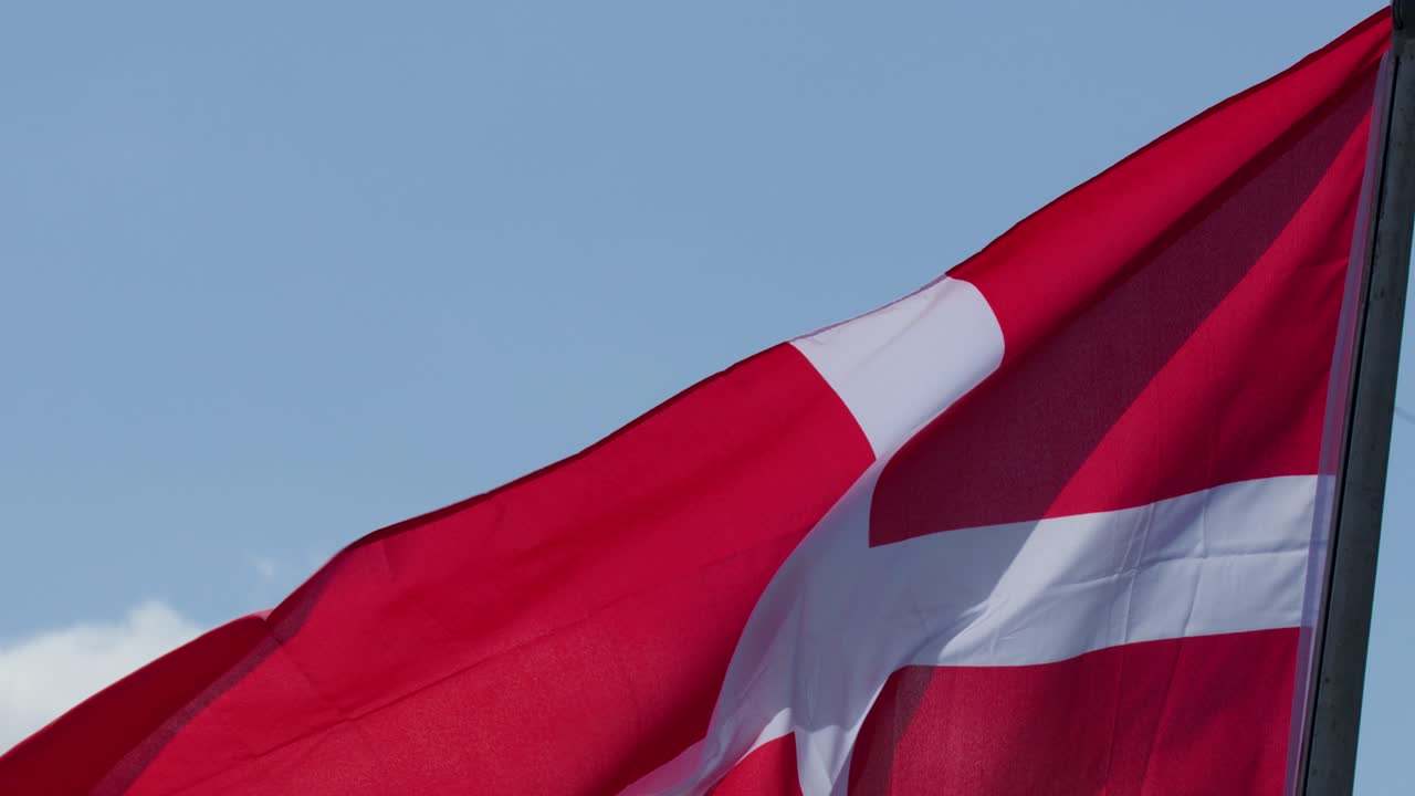 Rødt og hvidt korsflag blafrer dynamisk på flagstang, dagslys, klar himmel, udendørs omgivelser