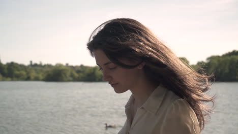 sunset portrait of an adorable and beautiful italian model walking next to a lake, wearing a transparent collar shirt, looking around, wandering and being free