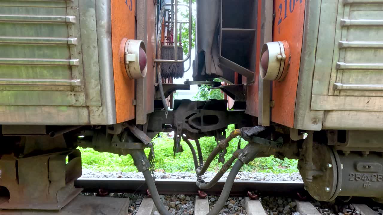 Close-up video of train coupling and wheel movement on tracks in Kanchanaburi, Thailand. Natural lighting highlights mechanical details