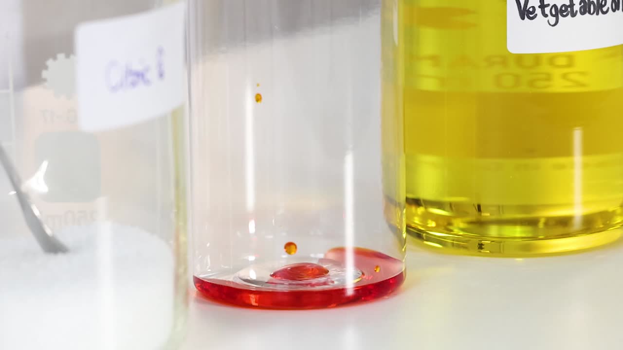 Observe red droplets interacting with oil and water in a clear container.