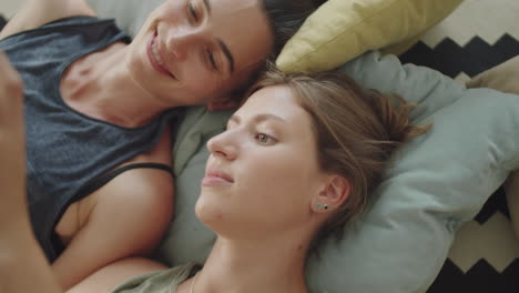 women lying on bed and using smartphone