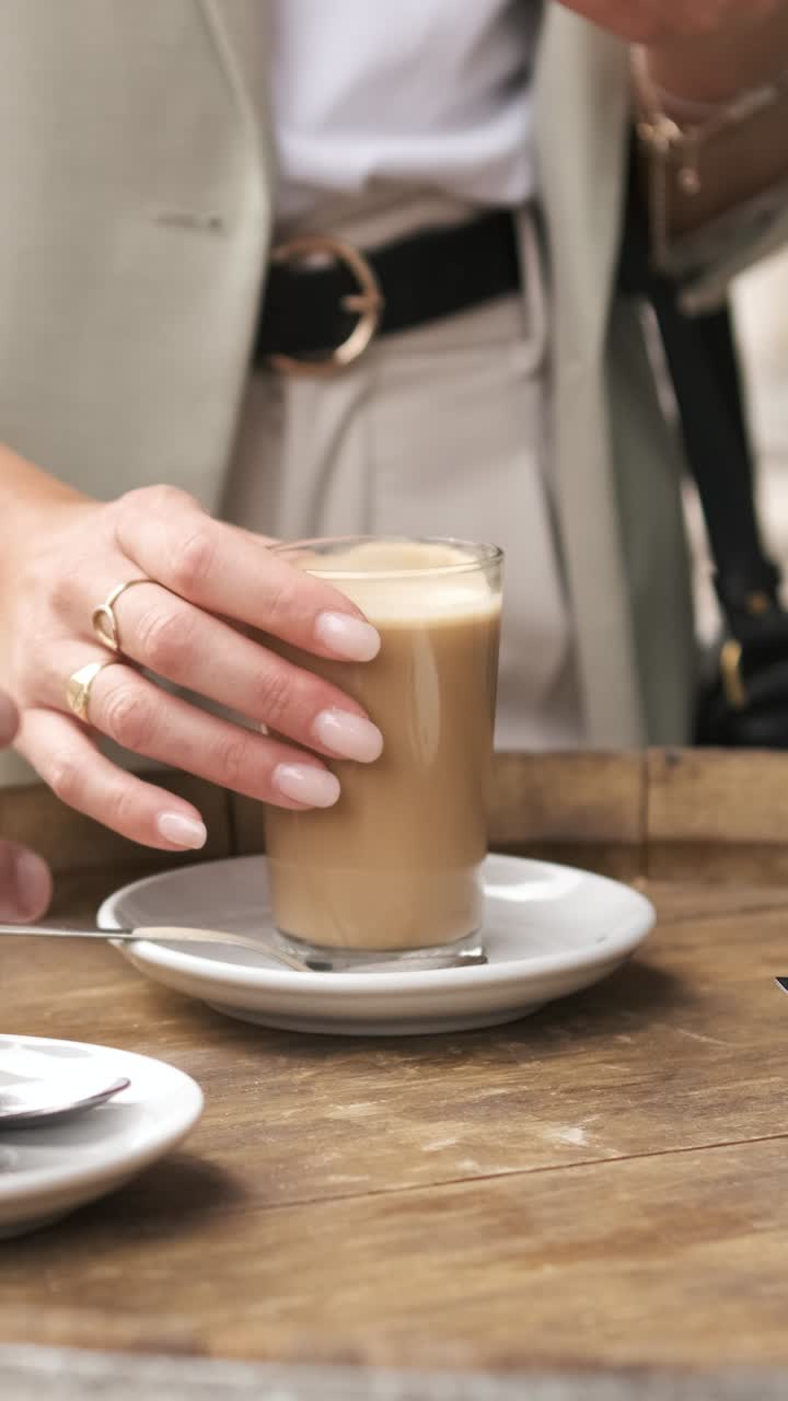 Businesswoman enjoying a relaxing moment while picking up a latte from a coffee shop table. Vertical