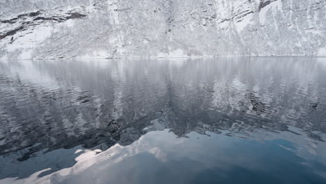 POV-video-of-a-ferry-ride-through-Geirangerfjord-in-winter,-featuring-stunning-views-of-snow-covered-mountains,-a-bright-sky,-and-reflections-in-the-fjord