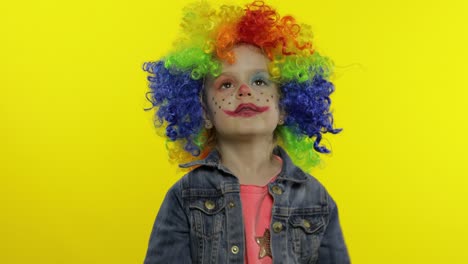 little child girl clown in colorful wig making silly faces. having fun, smiling, dancing. halloween