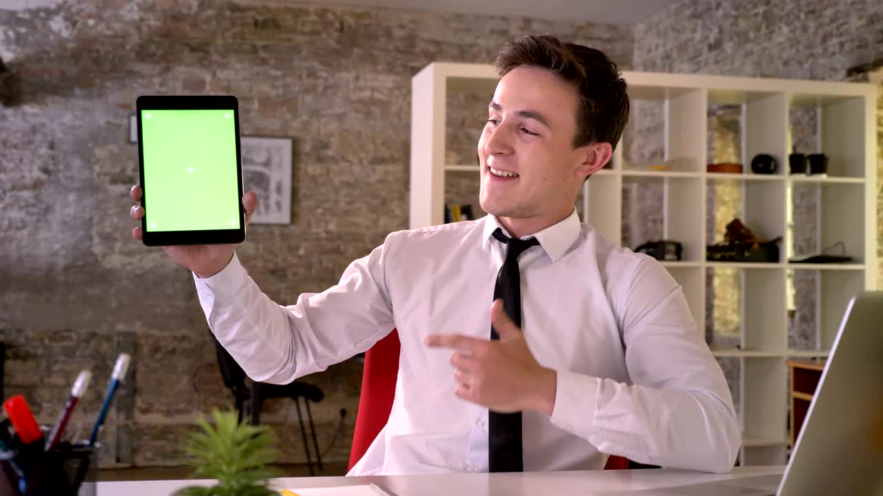 Young businessman is working with tablet in office, showing green screen, point on it, business concept, communication concept