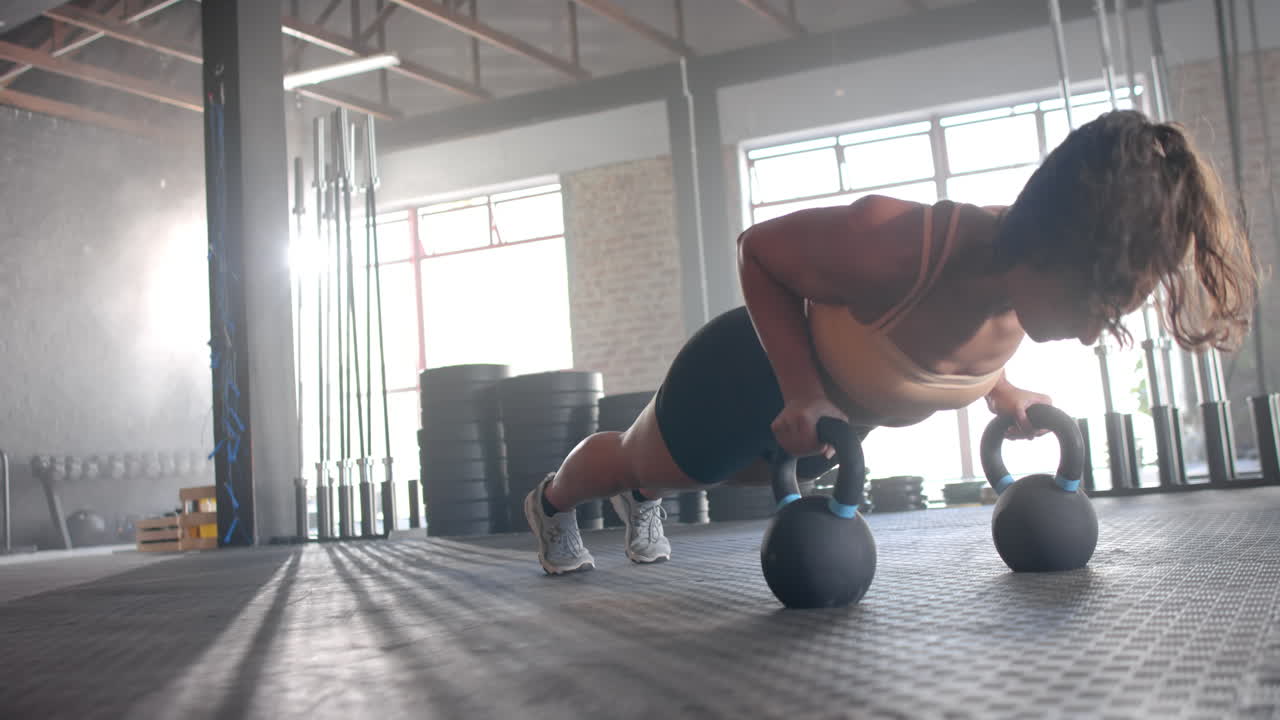 Performing push-ups using kettlebells, woman exercising in gym for fitness, copy space
