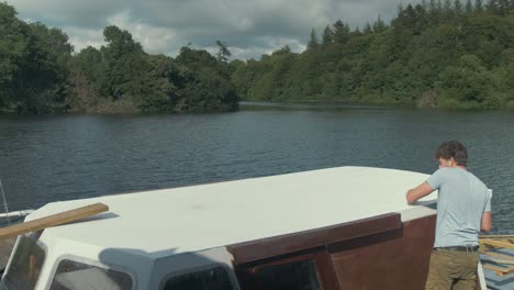 young man wipes dust off wooden boat roof before painting