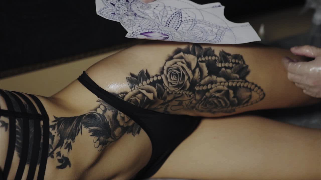 Woman getting a black and grey floral tattoo on her hip and thigh