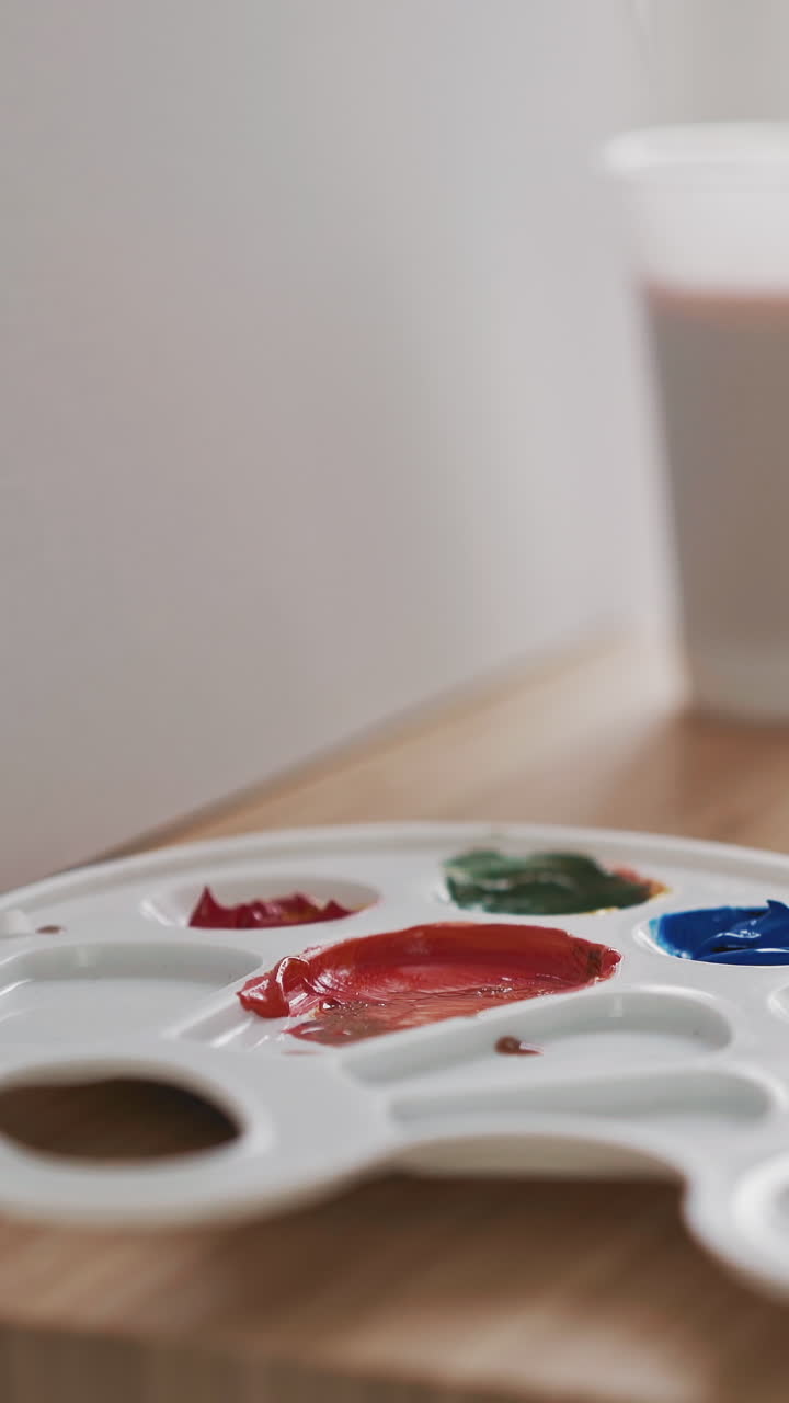 Woman artist takes dark green paint from palette with paintbrush drawing watercolor on white canvas sitting at wooden easel in art studio closeup