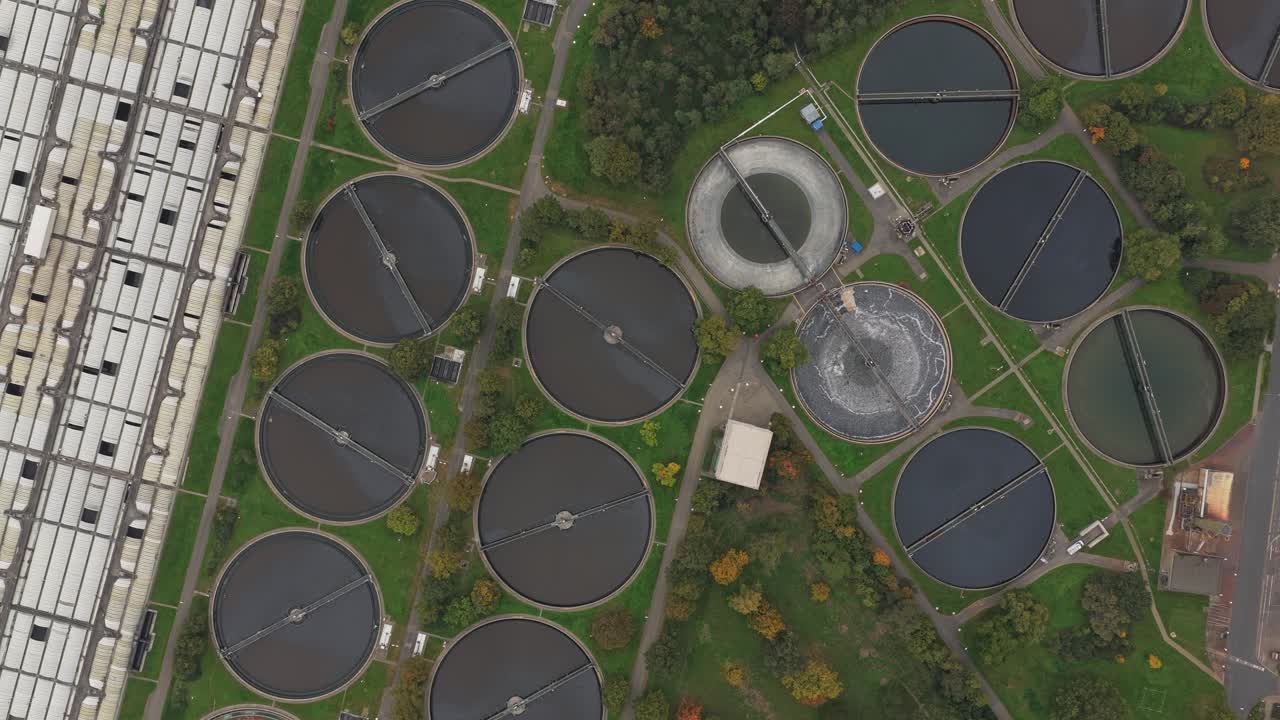 Aerial top down view showing a wastewater treatment plant with large circular sedimentation tanks processing sewage, demonstrating modern urban sanitation and environmental water management systems