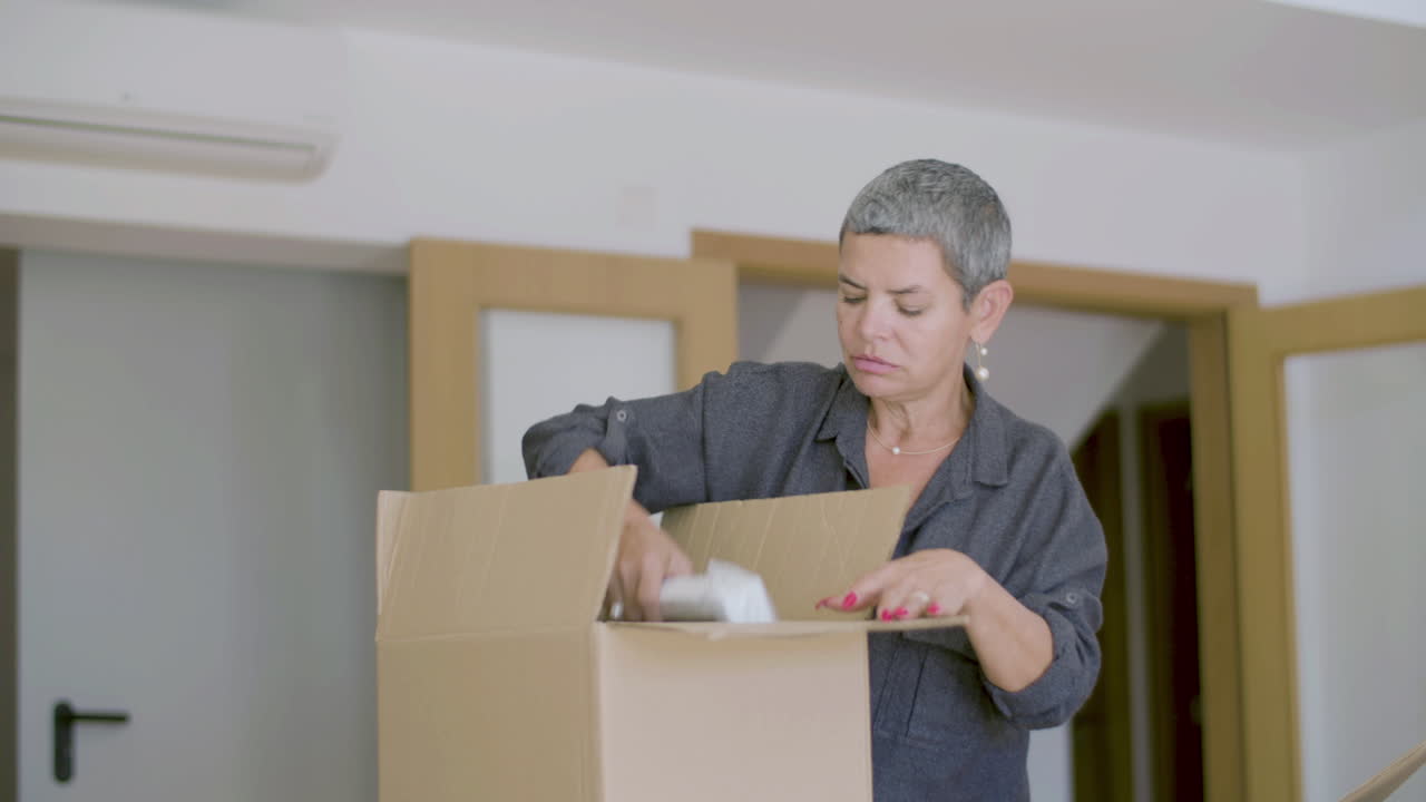 Mature woman unpacking carton boxes after moving to new house
