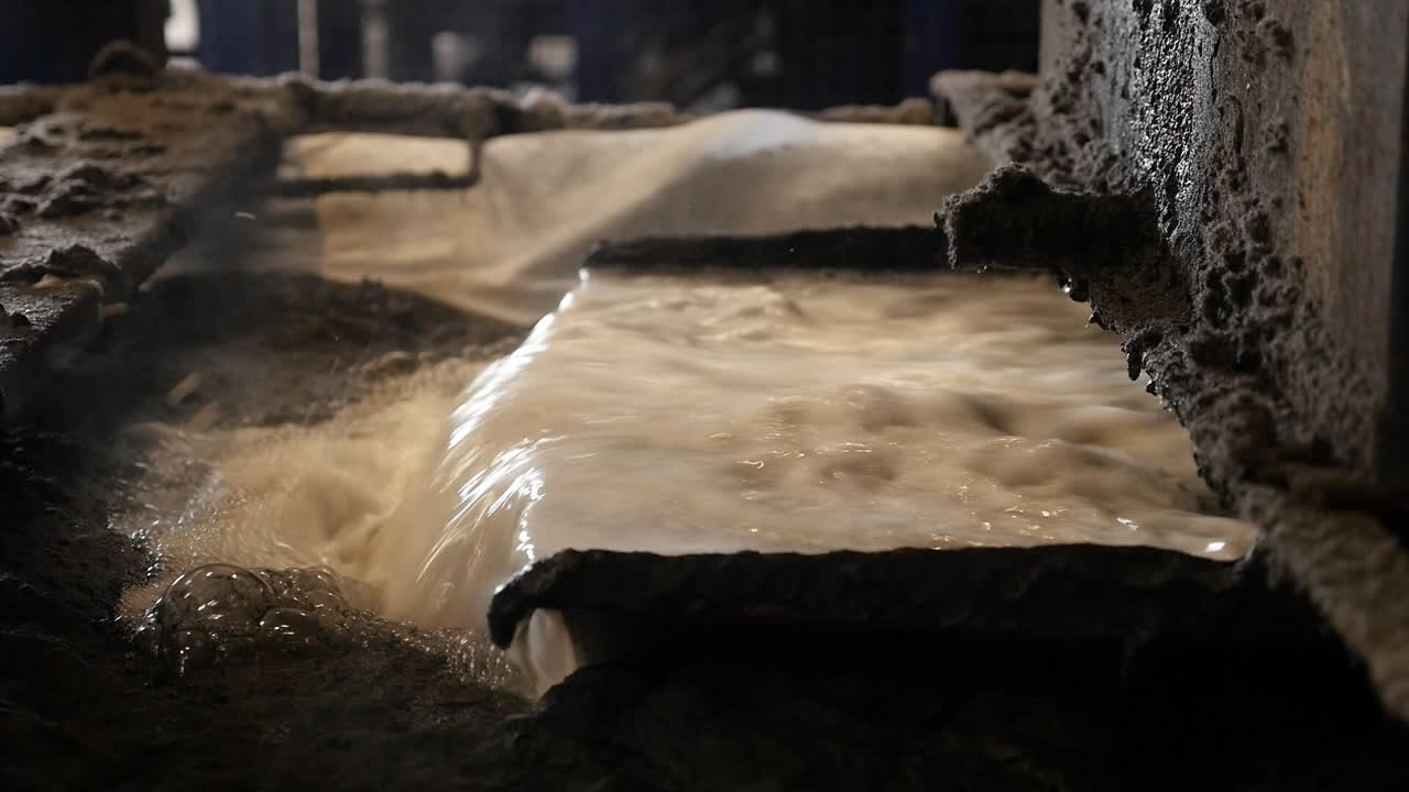 A stream of foamy, dirty wastewater flowing into a pipeline inside a tire recycling plant