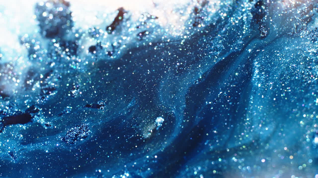 Swirling blue and white liquids create a cosmic effect with glittering textures, close-up macro view